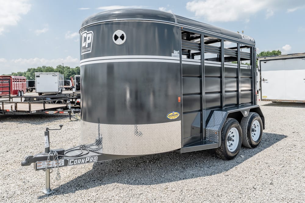 Grey double-axle livestock trailer with side slats on a gravel lot, front hitch visible and Diamond Plate ahead