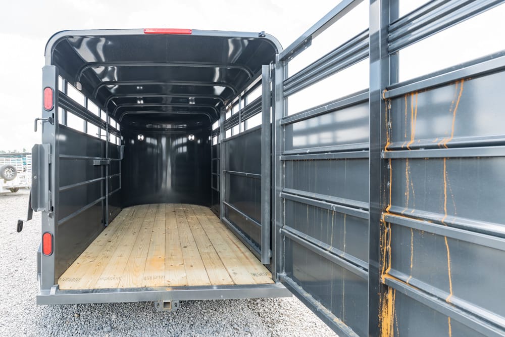 Empty dark metal livestock trailer with a wooden floor, open rear doors ready for loading animals.