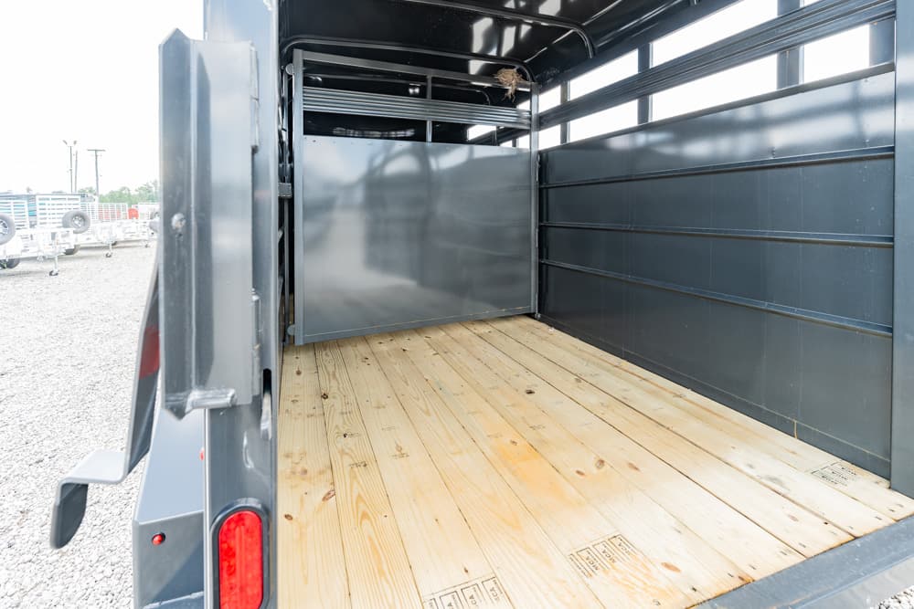 Interior of an empty metal trailer with a wooden plank floor and high gray side walls outside light visible at the rear door.