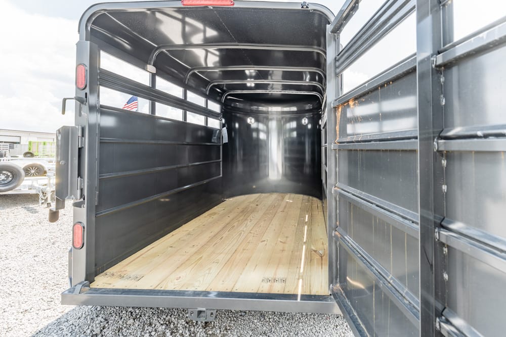 Open livestock trailer interior with wooden floor and black metal walls, daylight streaming in from open rear gate.