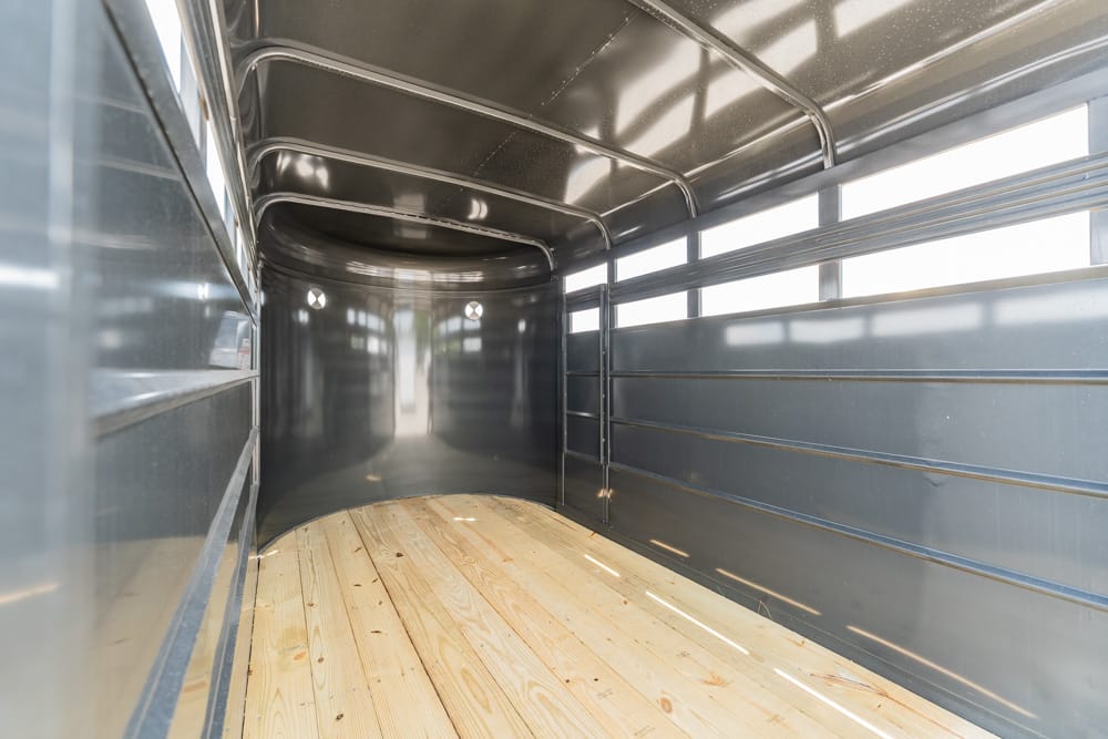 Interior of an empty metal truck trailer with wooden floor and curved walls, lit by daylight from side windows