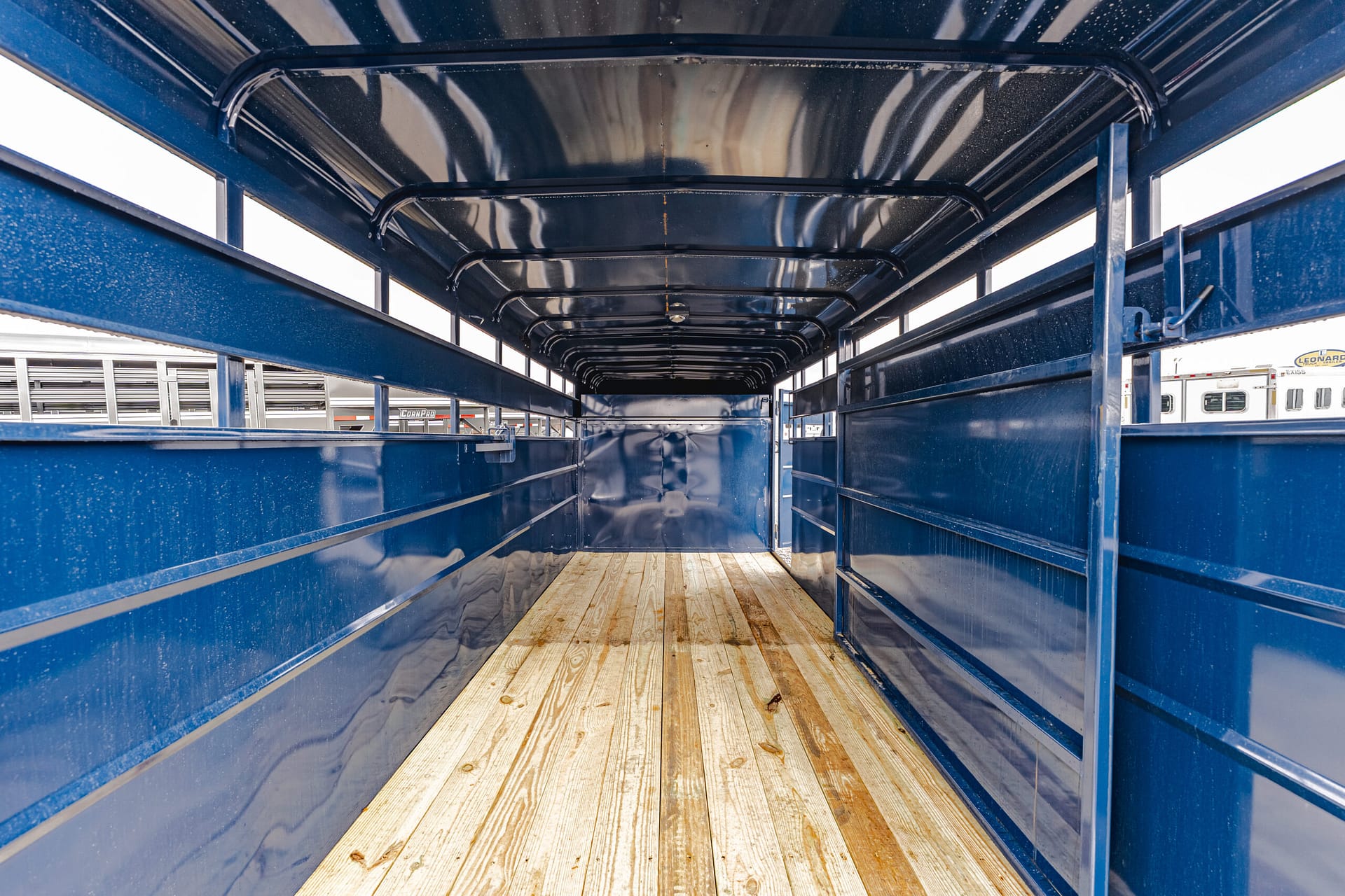 Interior of a long blue metal trailer with a wooden floor, viewed from the back toward the far end, empty.