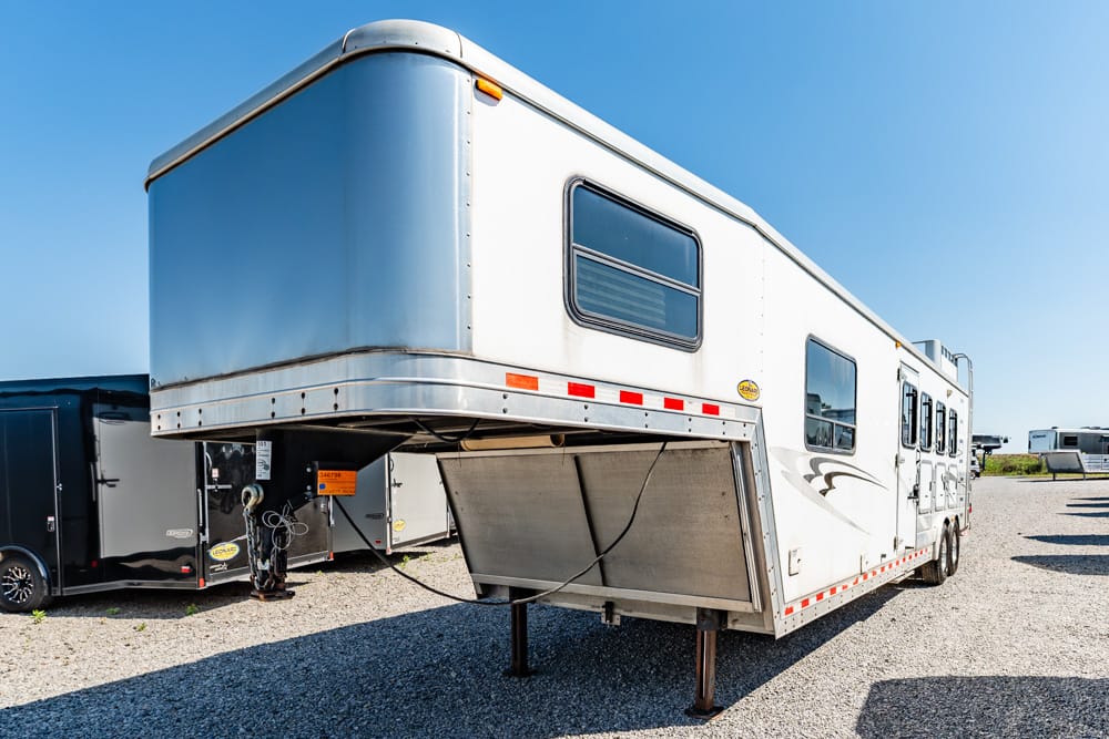 White gooseneck horse trailer with raised front section parked on gravel under a clear blue sky
