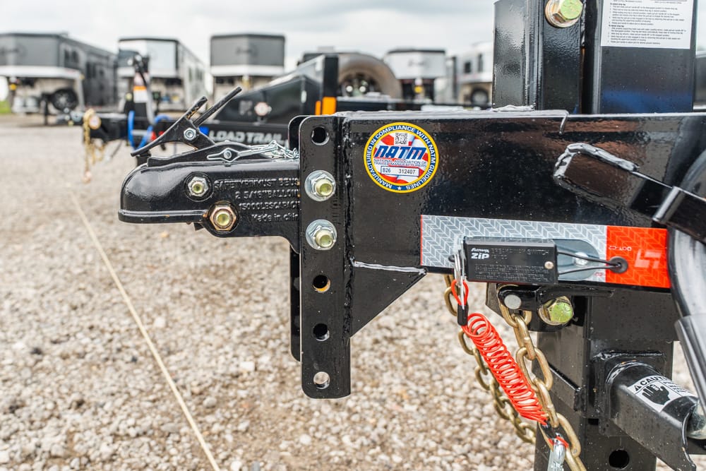 Close-up of a trailer hitch with bolts, safety chains, a red coiled lanyard, and a padlock on a black metal frame.