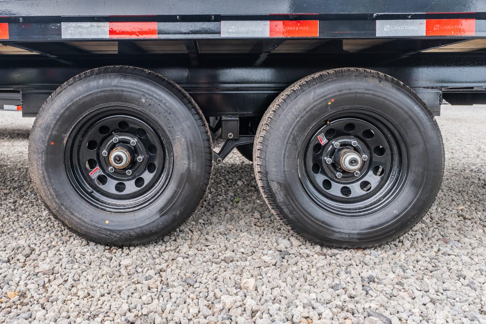 Dual-axle trailer wheels with black rims on a gravel surface.