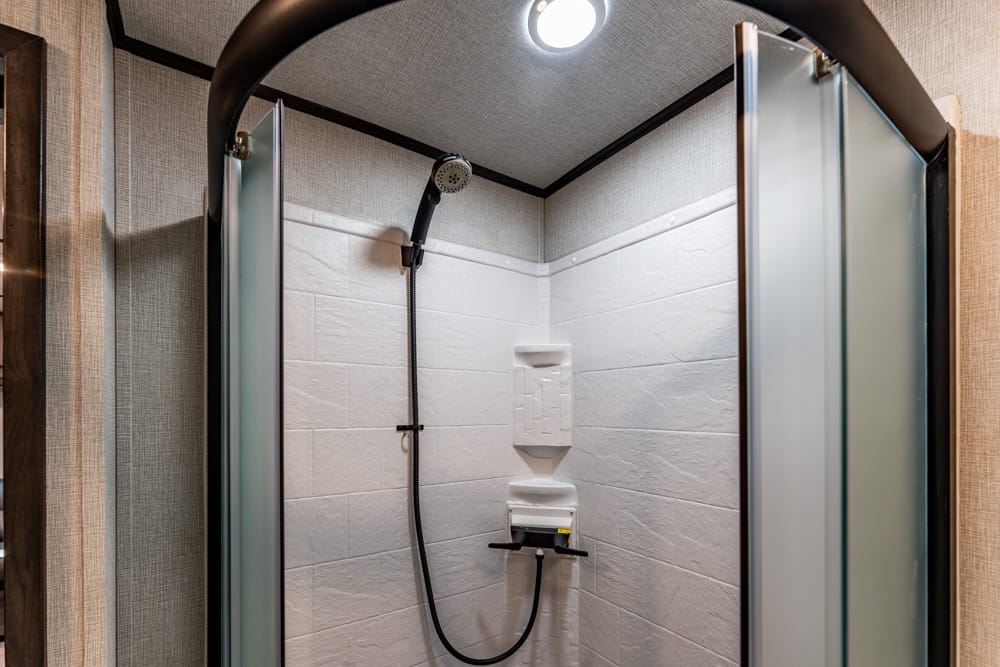 Shower stall with frosted glass doors, white tiled walls, and a handheld showerhead on a rail shelf area.