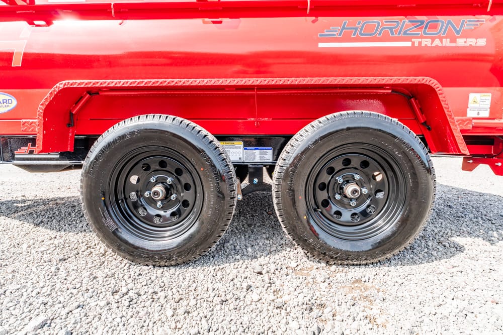 Red Horizon trailer with dual axles and black steel wheels on a gravel surface, side view.