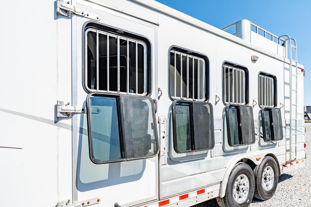 White horse trailer with barred windows along its side parked on a gravel lot.