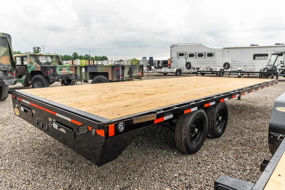 Flatbed trailer with a wooden deck and dual rear axles parked on a gravel lot.