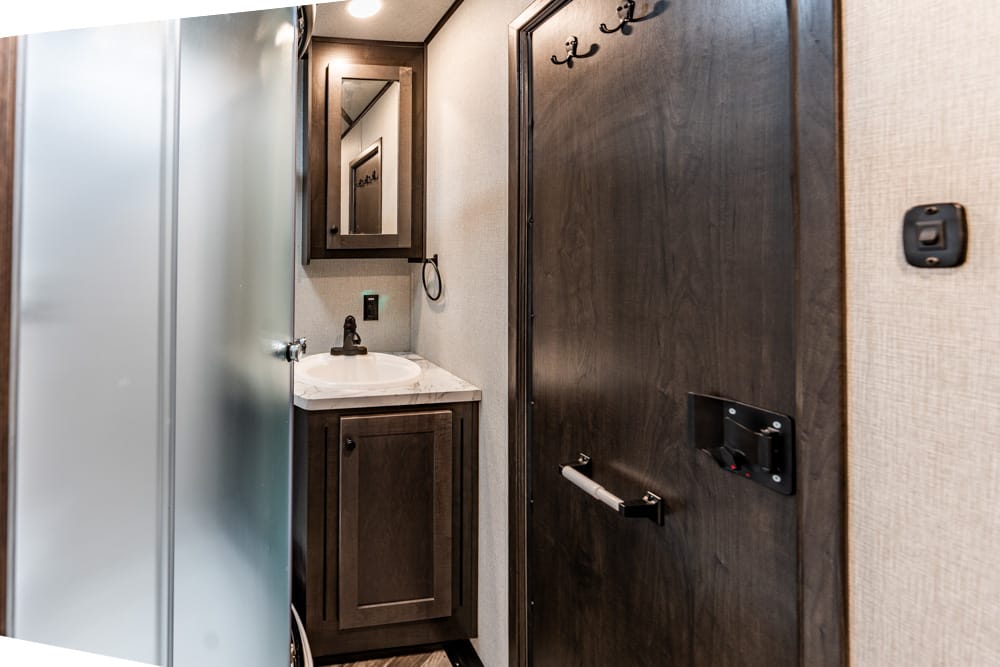 Compact RV bathroom with dark wood vanity, white sink, and frosted shower door on the left.