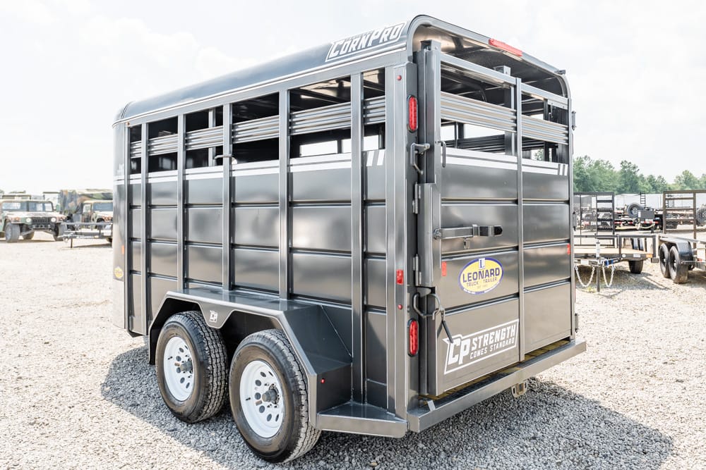 Dark gray two-axle livestock trailer on a gravel lot, with side ventilation slats and rear double doors.]