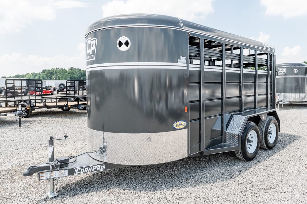 Gray livestock trailer with open side gates and diamond-plate nose, parked on a gravel lot.