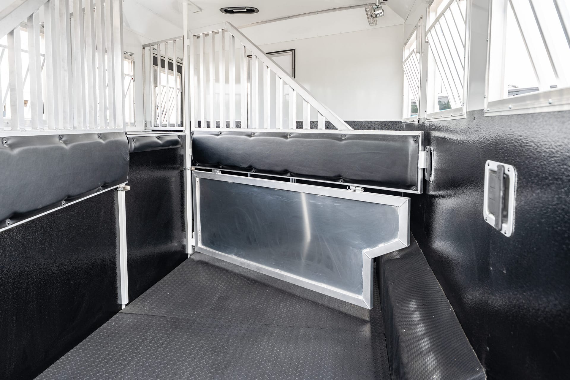 Interior of a white horse trailer with vertical metal dividers and black padded walls separating stalls.