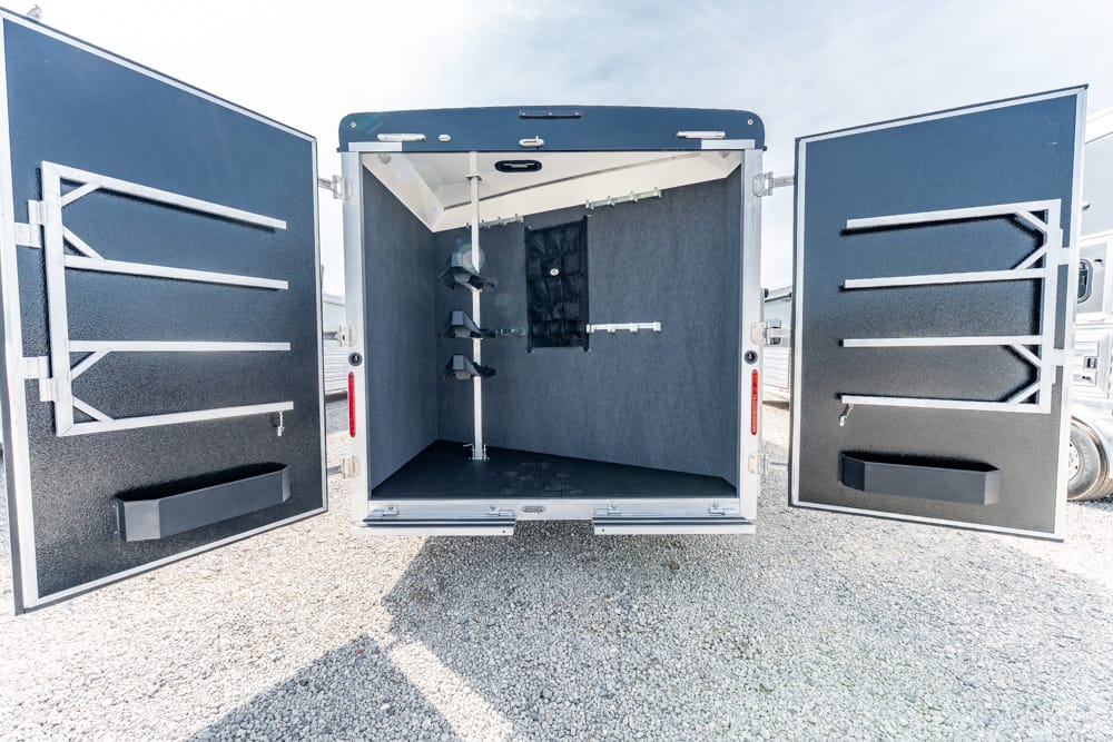 Open cargo trailer interior with built-in racks and hooks on gray walls, rubber floor.