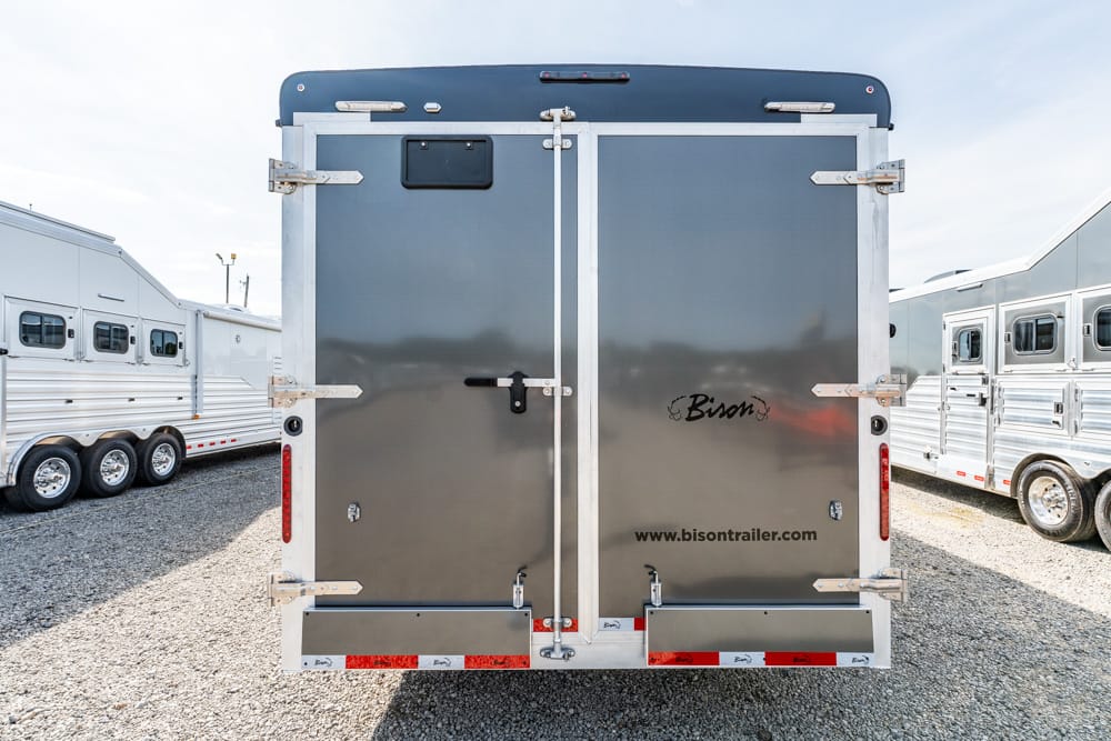 Rear view of a gray double-door horse trailer with metal latches, Bison logo, and www.bisontrailer.com on a gravel lot among other trailers