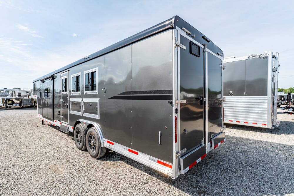 Black dual-axle horse trailer with silver trim on a gravel lot, adjacent trailers in the background.