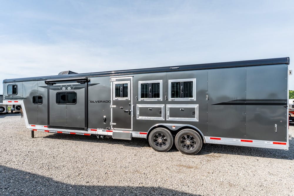 Long gray horse trailer with living quarters, doors and windows, parked on a gravel lot (dual-axle).