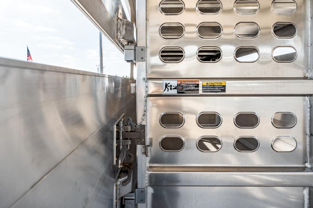 Inside of a metal trailer with vented panels, a latch and warning labels; an American flag is visible outside the open side.