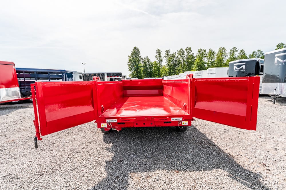 Red dump trailer with side doors wide open in a gravel lot.