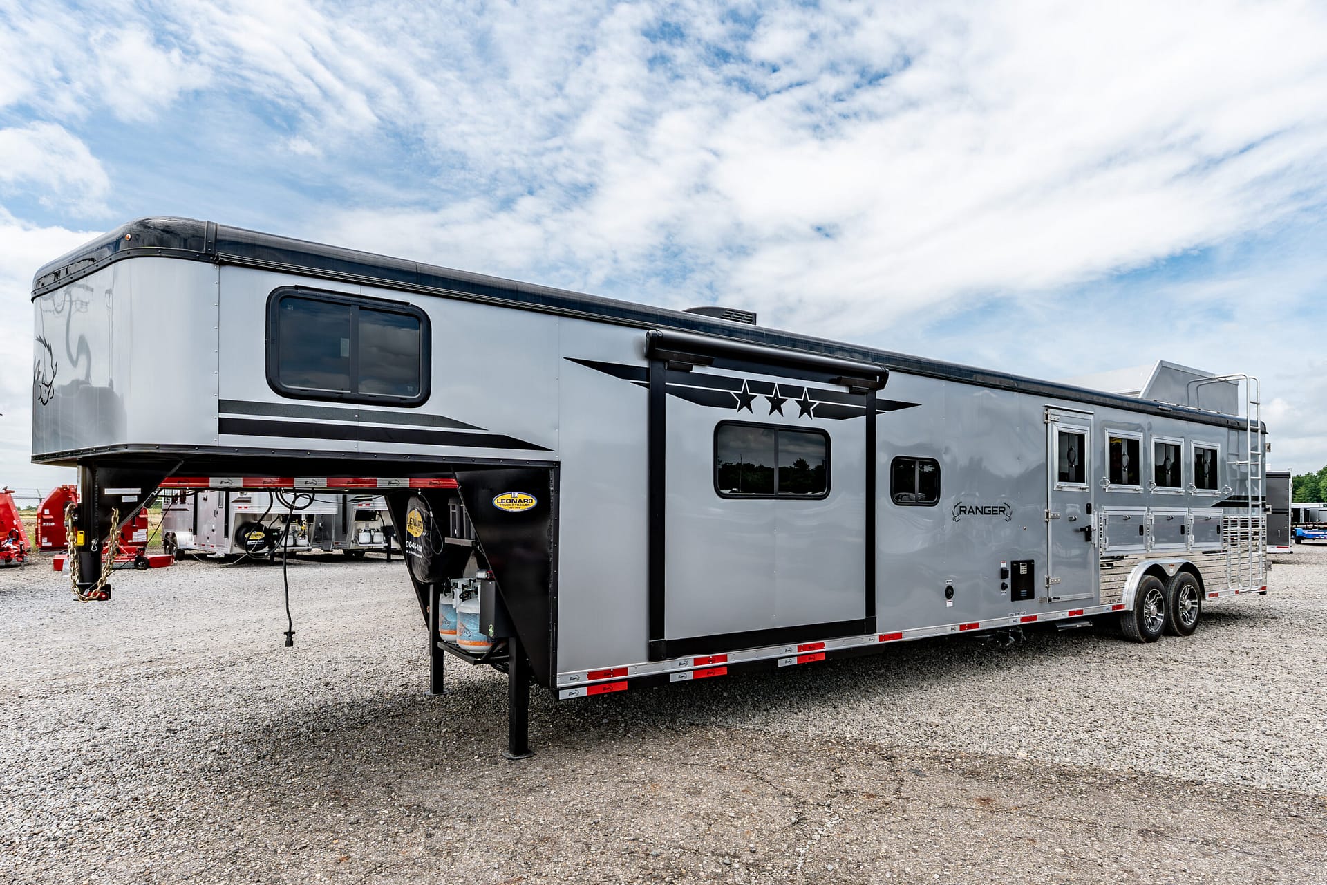 Large grey and black travel trailer parked on a gravel lot beneath a blue sky and wispy clouds