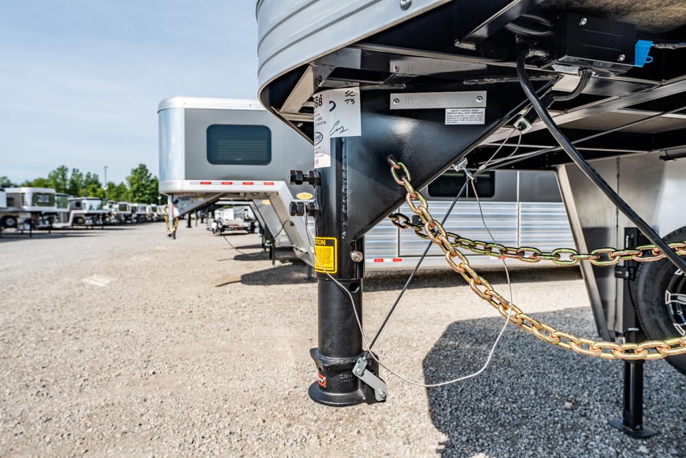 Close-up of a fifth-wheel trailer hitch with safety chains and wiring, attached to a black support post in a lot of RVs.