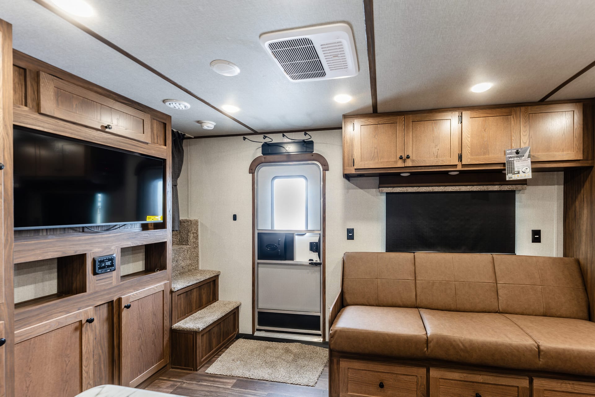 Interior of a recreational vehicle showing built-in wooden cabinets, a wall-mounted TV, and a brown leather-like sofa.