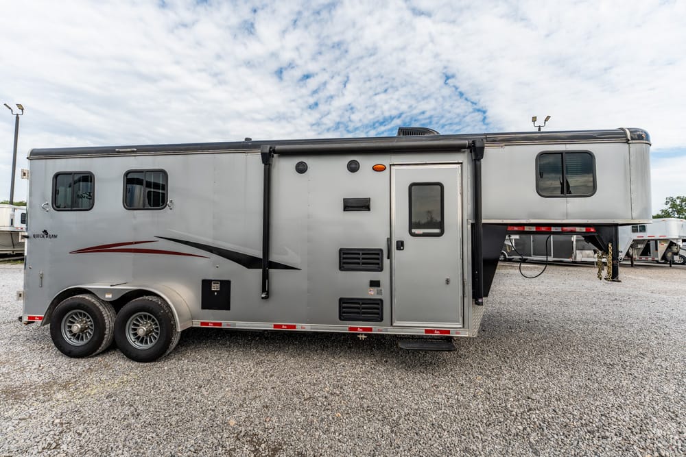 Silver horse trailer with two axles parked on gravel, side entry door and small windows along the side.