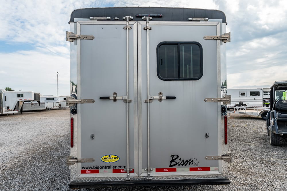 Back of a gray horse trailer with two vertical doors, small window, metal latches, and brand logos (Bison, Leonard trailer).