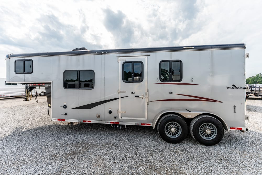 Silver aluminum horse trailer with two axles and red/black decals, parked on a gravel lot.