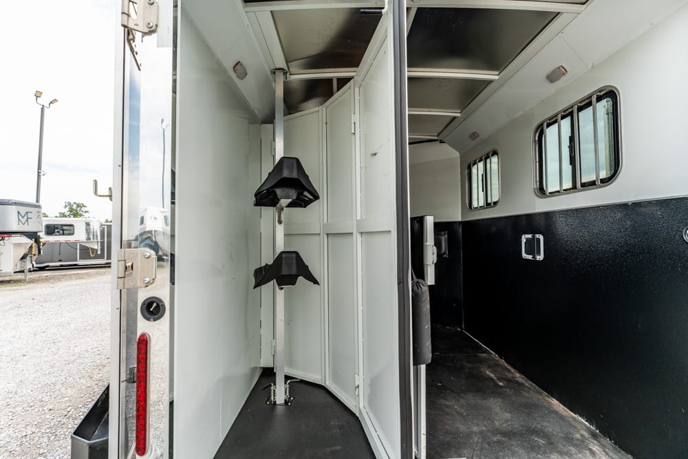 Interior of a horse trailer with white divider panels, a black rubber floor, and saddle racks mounted on a vertical rail.