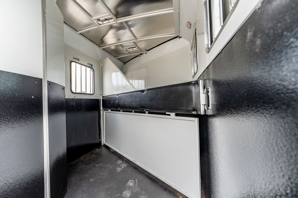 Interior of a metal transport trailer with a black padded divider along the wall and a small window at the far end.