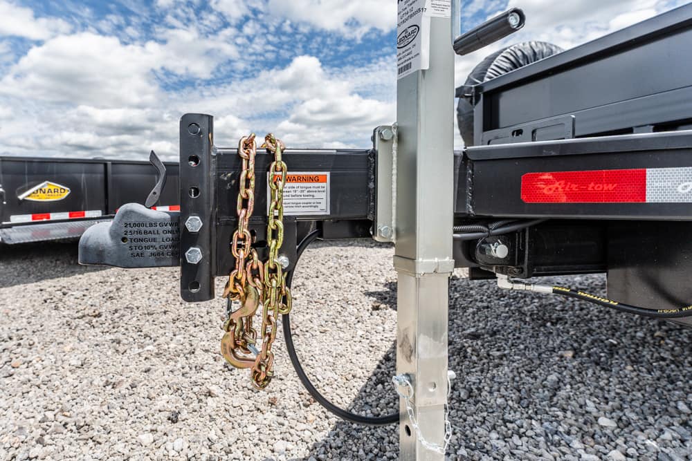 Close-up of a trailer hitch and safety chains attached to a vertical hitch post on a gravel lot with a blue sky above.