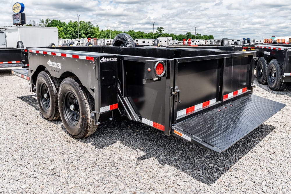 Black tandem-axle dump trailer with ramp lowered, parked on a gravel lot in a trailer yard.