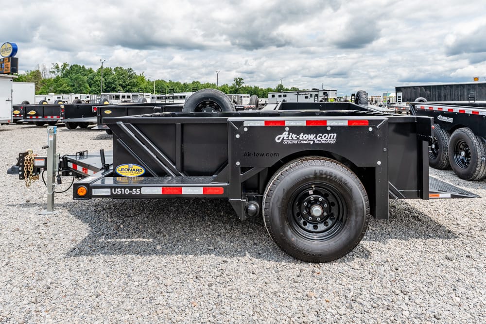 Black Air-Tow utility trailer with spare tire, hitch, and safety chains on a gravel lot.