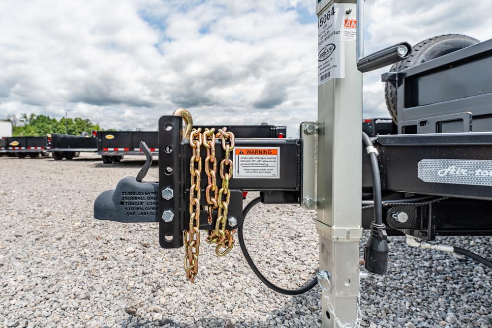 Close-up of a trailer hitch with safety chains and a warning label on a metal frame.
