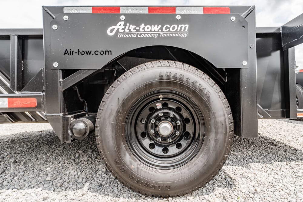 Close-up of a heavy-duty trailer tire and wheel on a black Air-tow trailer, with Load Star tire branding over gravel ground.
