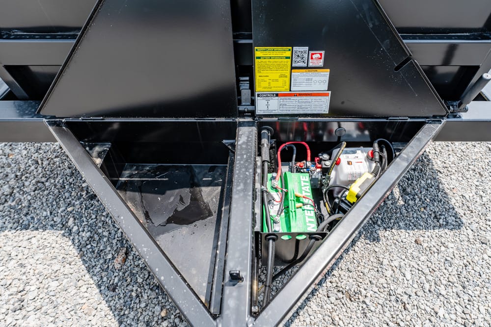 Open storage bay on a trailer with a green Interstate battery and wiring inside.