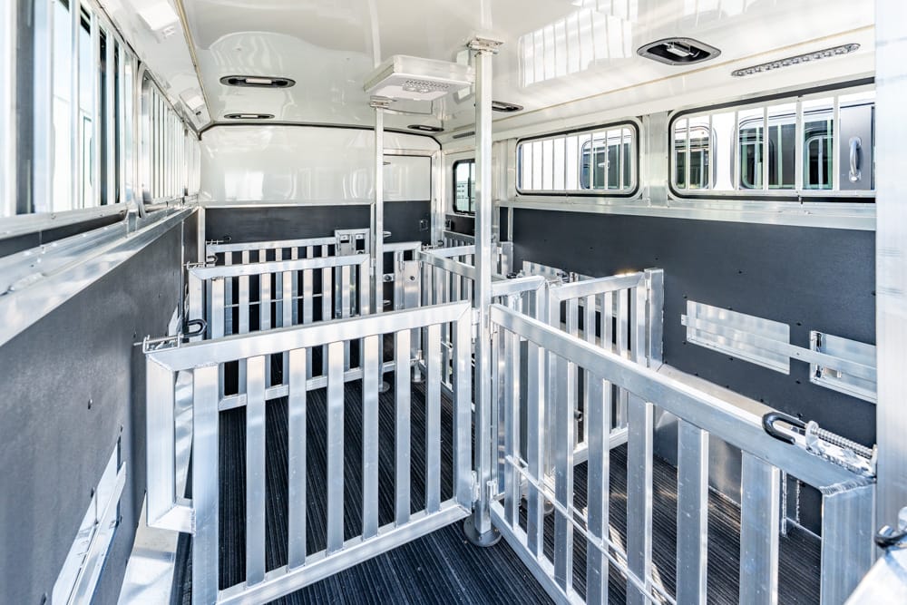 Interior of a horse trailer with multiple metal stalls and dividers, rubberized flooring, and side windows for ventilation and light.