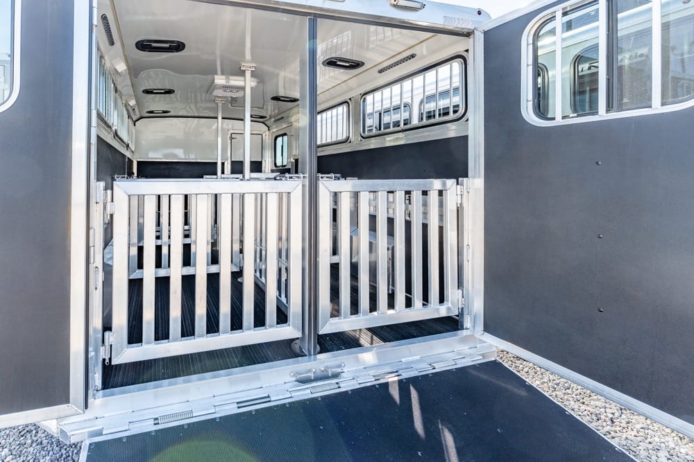 Interior of a dual-horse trailer with metal dividing gates, a non-slip floor, and side windows; rear ramp lowered for loading