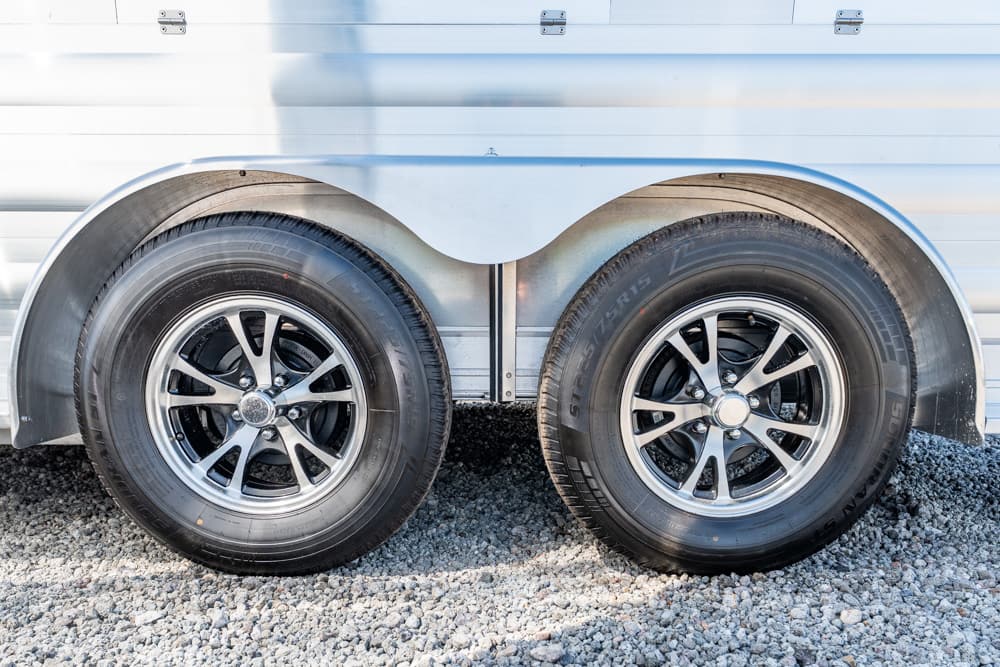Dual-axle trailer with two tires and chrome rims, curved metal fenders, on gravel ground.