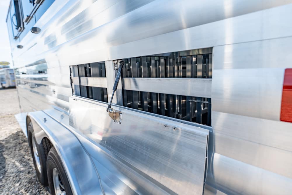 Close-up of a shiny aluminum truck trailer with an open side vent panel and a latch on the hinged door