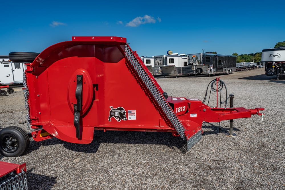 Red round-bale baler on a gravel lot with trailers in the background.