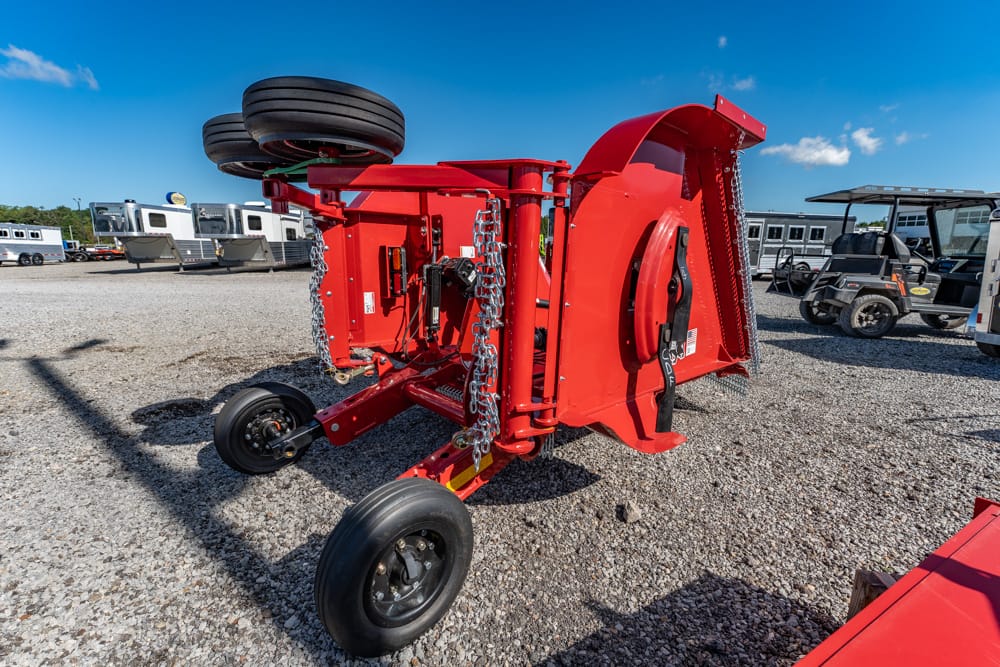 Red folded farming implement on a gravel lot with dual wheels and hanging chains, parked under a clear blue sky
