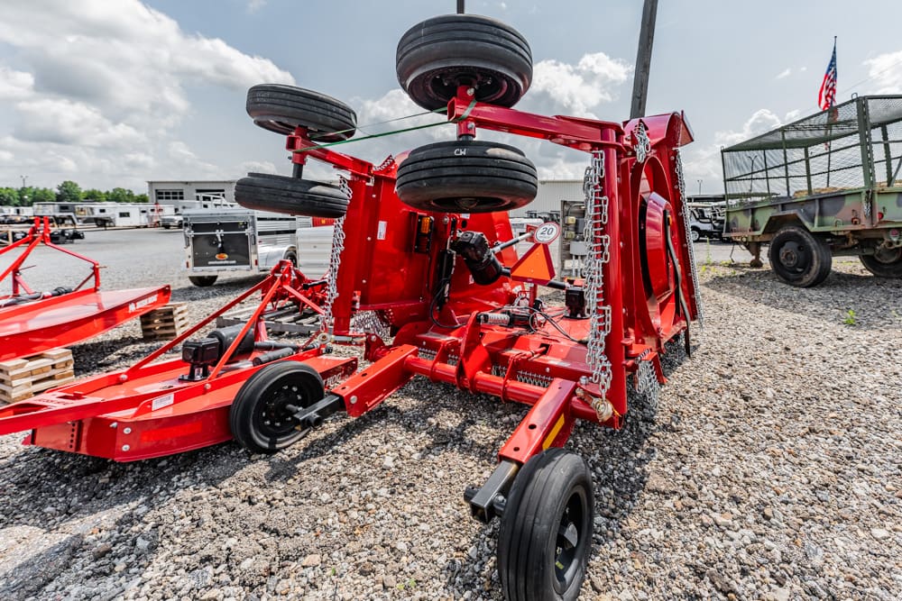 Red agricultural implement with large wheels and hydraulic components on a gravel lot, likely at a farm equipment yard.