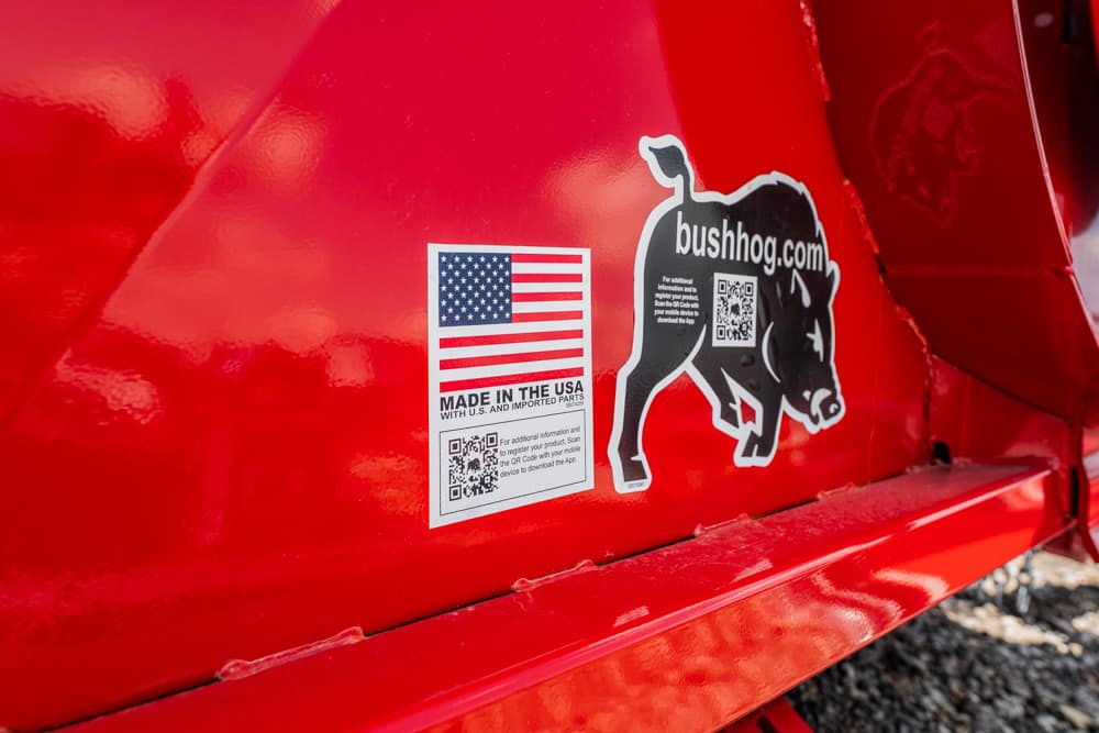 Close-up of red metal equipment with stickers: American flag and 'Made in the USA' label next to a Bush Hog bulldog logo.