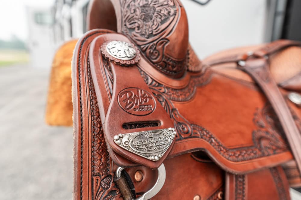 Close-up of a brown leather western saddle with decorative tooling and silver conchos.