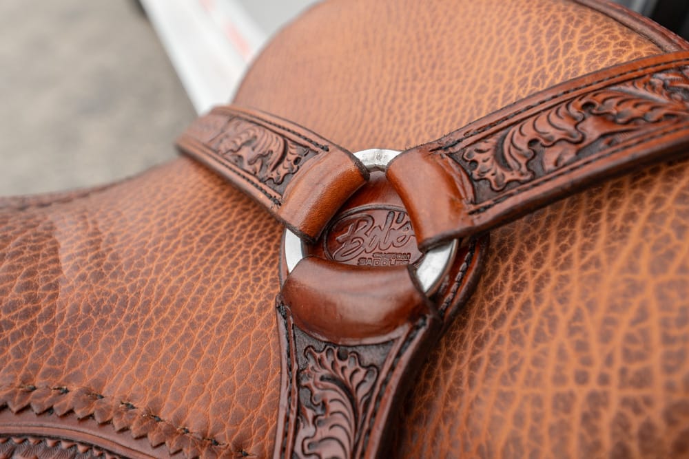 Close-up of a brown leather bag with stitched patterns and decorative embossed straps.