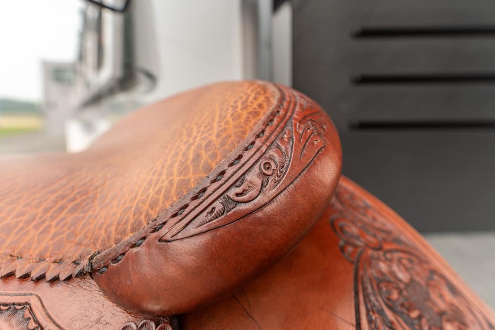 Close-up of a brown leather saddle with decorative tooling and stitching.