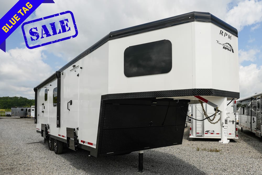 White gooseneck travel trailer on a gravel lot with a bold blue SALE stamp and Bluetag banner in the corner, ready for sale.