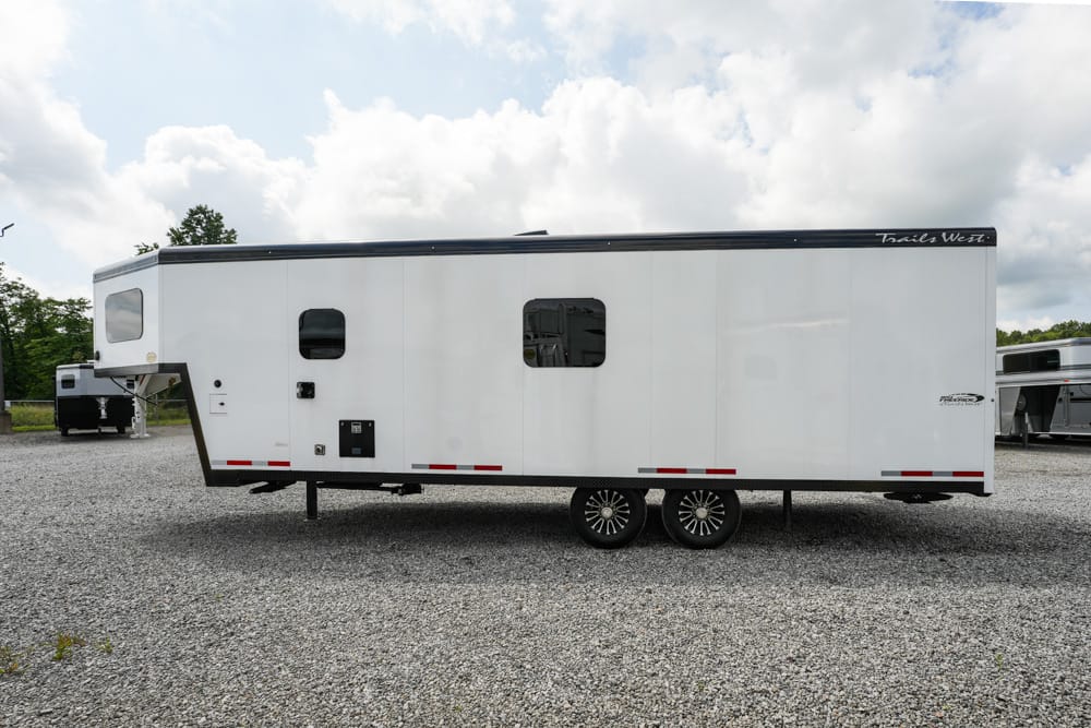 White two-axle gooseneck trailer parked on a gravel lot under a partly cloudy sky.